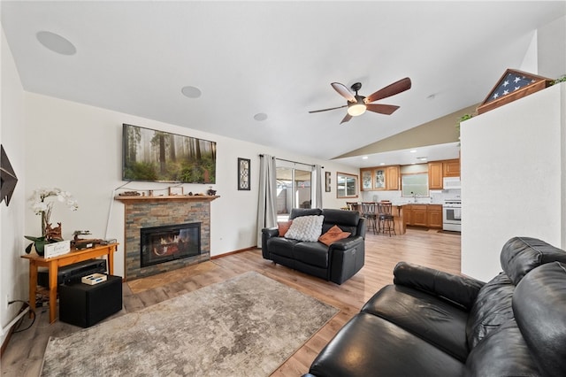 living room with light wood finished floors, lofted ceiling, ceiling fan, a stone fireplace, and baseboards