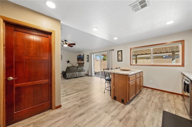 kitchen with visible vents, a kitchen breakfast bar, open floor plan, a peninsula, and light wood-type flooring