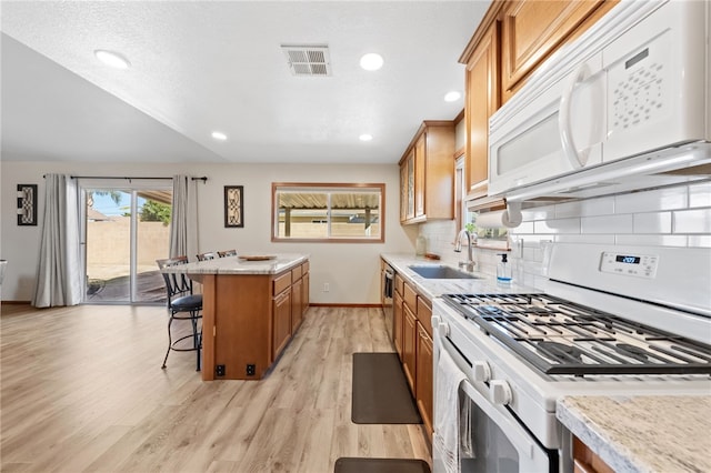 kitchen with white appliances, a breakfast bar, a sink, visible vents, and a kitchen island