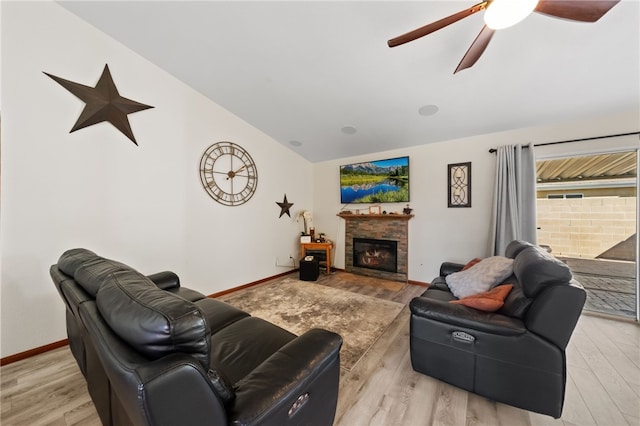 living area featuring lofted ceiling, light wood finished floors, baseboards, and a glass covered fireplace