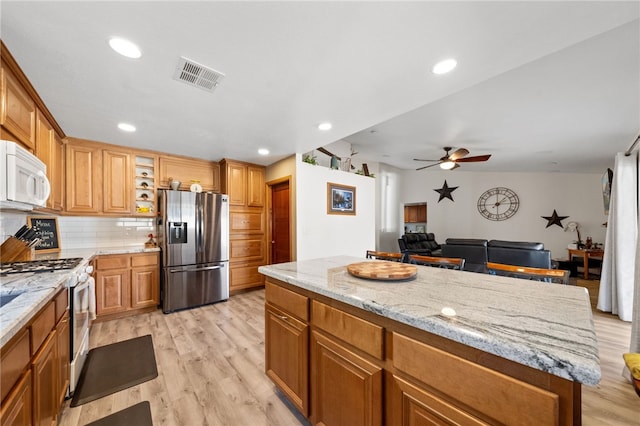 kitchen featuring white appliances, a kitchen island, visible vents, and brown cabinetry