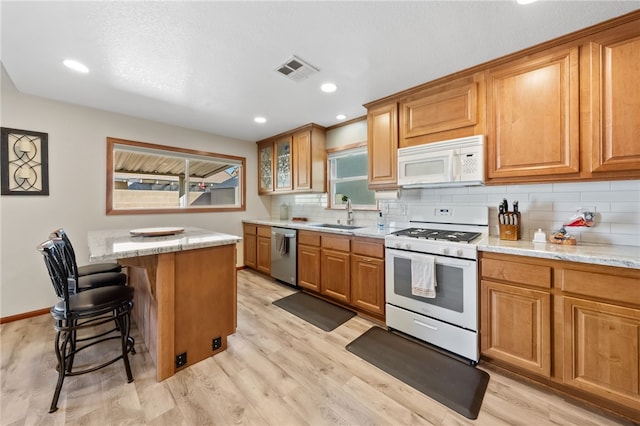 kitchen with brown cabinets, a breakfast bar area, visible vents, a sink, and white appliances