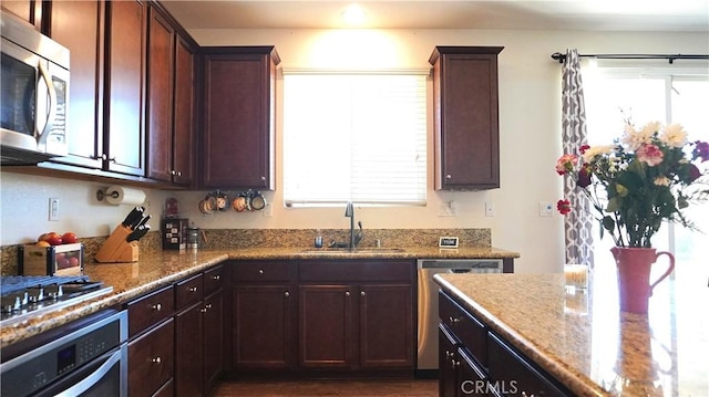 kitchen with stainless steel appliances, a sink, and light stone counters