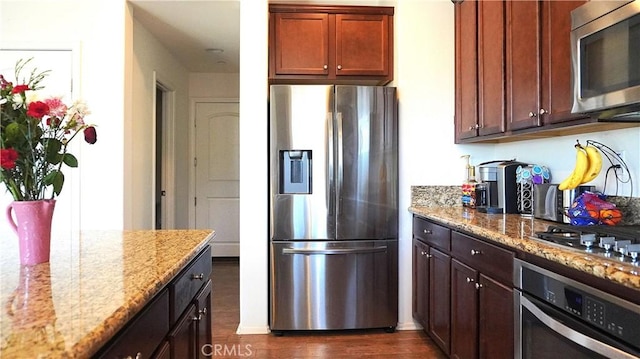 kitchen with stainless steel appliances, light stone counters, and dark wood-style flooring