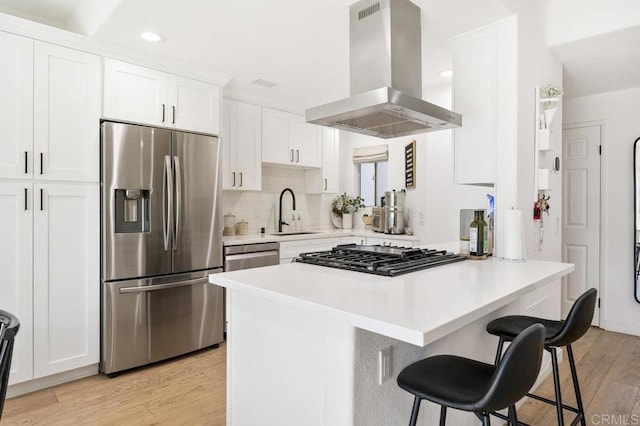 kitchen featuring a breakfast bar, a sink, white cabinetry, appliances with stainless steel finishes, and island exhaust hood