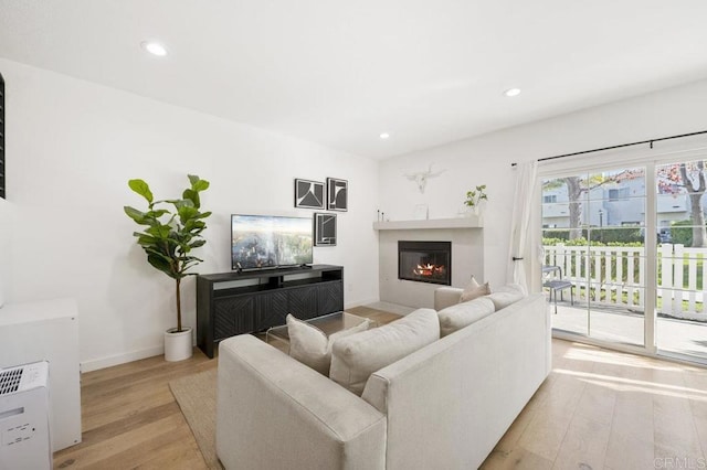 living area featuring light wood finished floors, baseboards, a glass covered fireplace, and recessed lighting