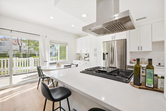 kitchen with white cabinets, island exhaust hood, appliances with stainless steel finishes, and light countertops