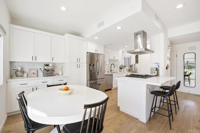 kitchen featuring island exhaust hood, stainless steel appliances, light countertops, a sink, and a peninsula