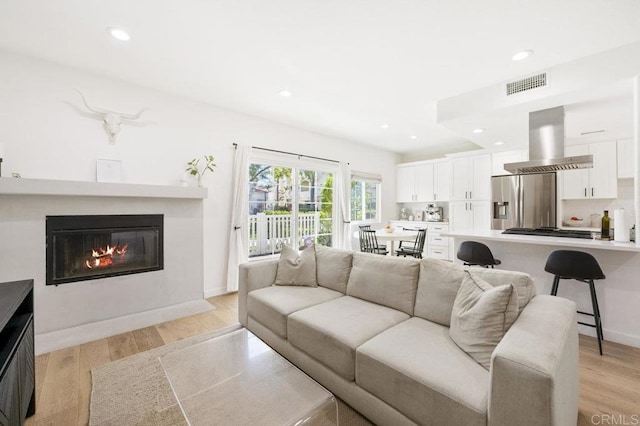 living room with light wood finished floors, a fireplace with flush hearth, visible vents, and recessed lighting