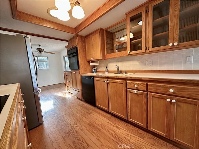 kitchen with black appliances, glass insert cabinets, light countertops, and brown cabinetry