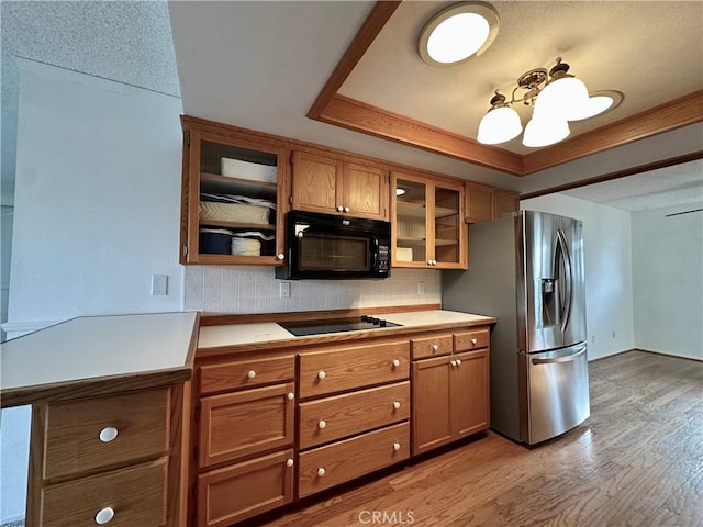 kitchen with light wood-style floors, light countertops, brown cabinets, black appliances, and a raised ceiling