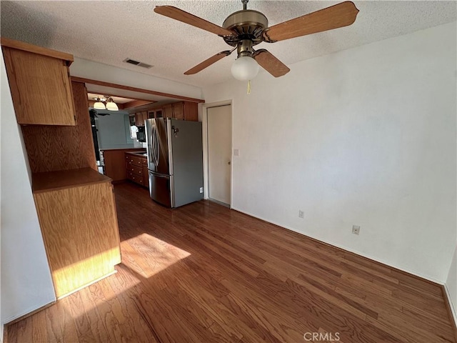 interior space featuring a ceiling fan, dark wood-style flooring, visible vents, and a textured ceiling