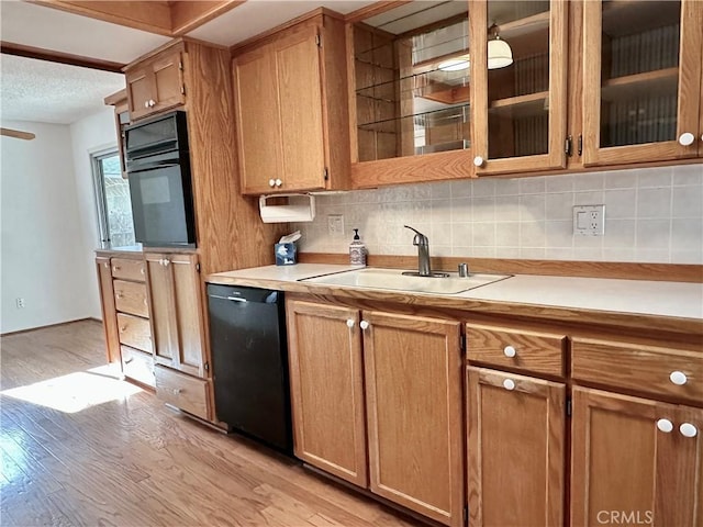 kitchen featuring a sink, black appliances, light countertops, and glass insert cabinets