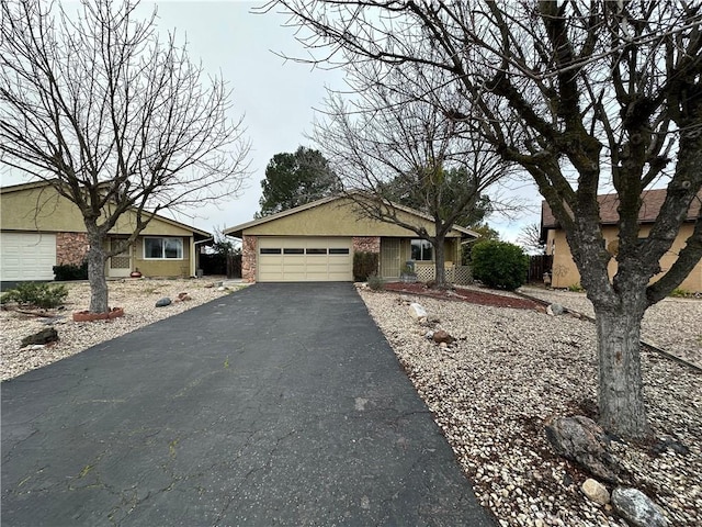 ranch-style house featuring a garage, brick siding, driveway, and stucco siding