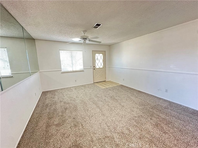 carpeted empty room with a textured ceiling, ceiling fan, and visible vents