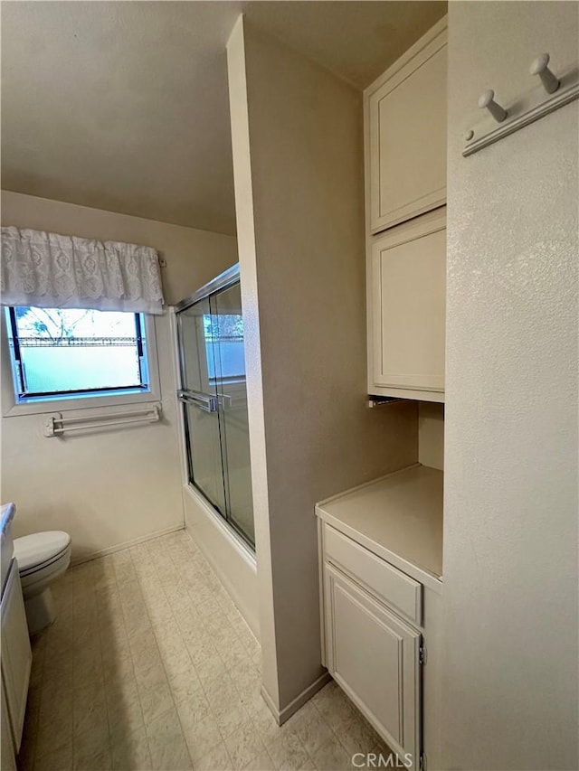 full bath featuring shower / bath combination with glass door, toilet, vanity, baseboards, and tile patterned floors