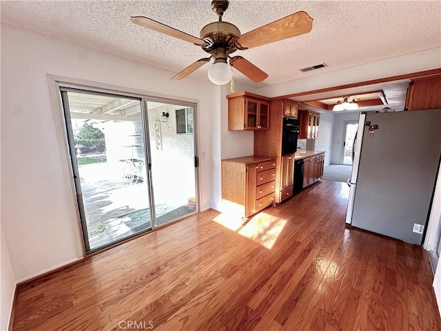 kitchen featuring visible vents, glass insert cabinets, dark wood-type flooring, light countertops, and black appliances