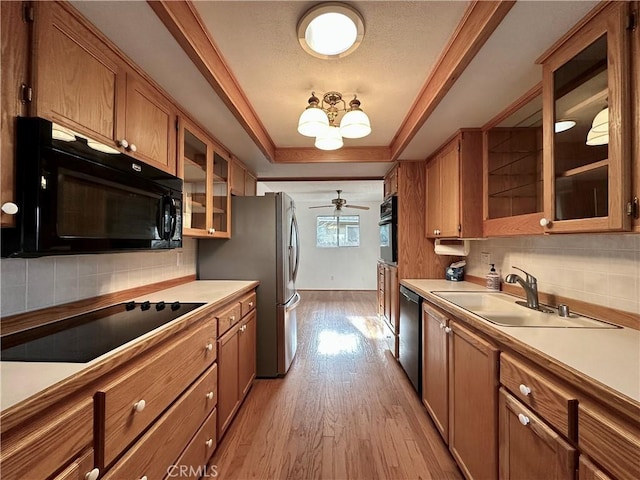 kitchen with light countertops, black appliances, a tray ceiling, and brown cabinetry