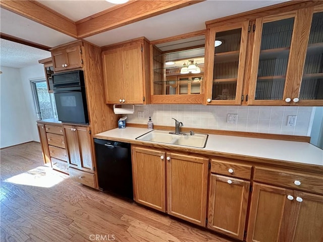 kitchen with brown cabinets, light countertops, glass insert cabinets, a sink, and black appliances