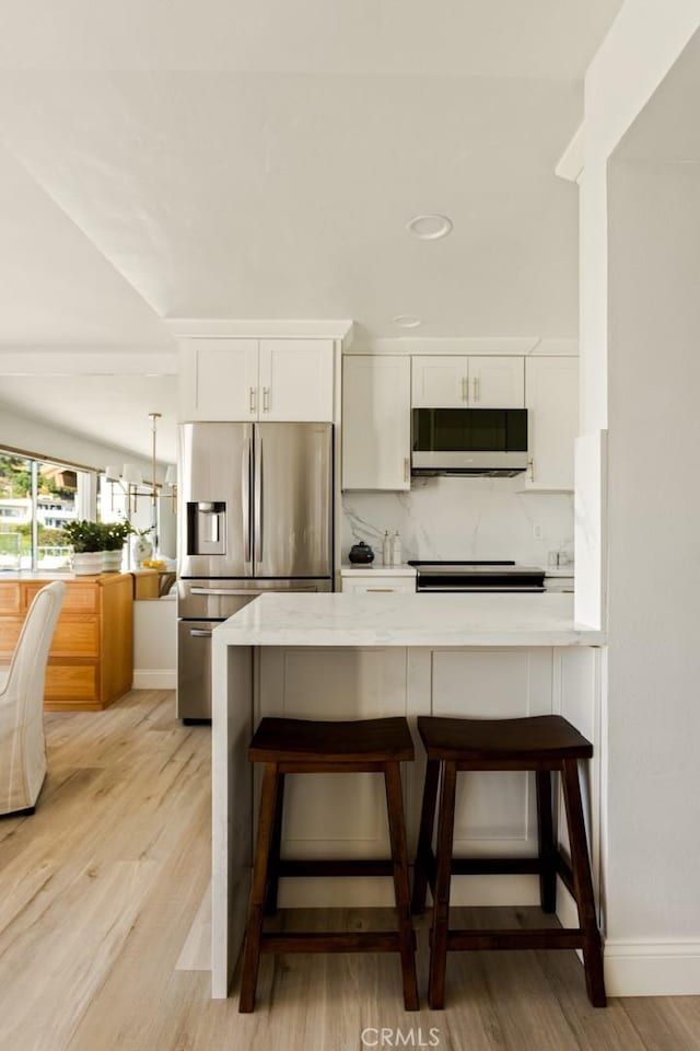 kitchen featuring a breakfast bar, light wood finished floors, stainless steel fridge, and white cabinets