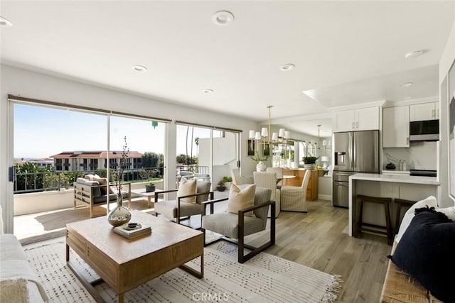 living area with recessed lighting, plenty of natural light, light wood-style flooring, and an inviting chandelier