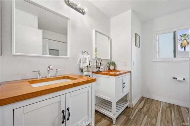 full bath with baseboards, two vanities, a sink, and wood finished floors