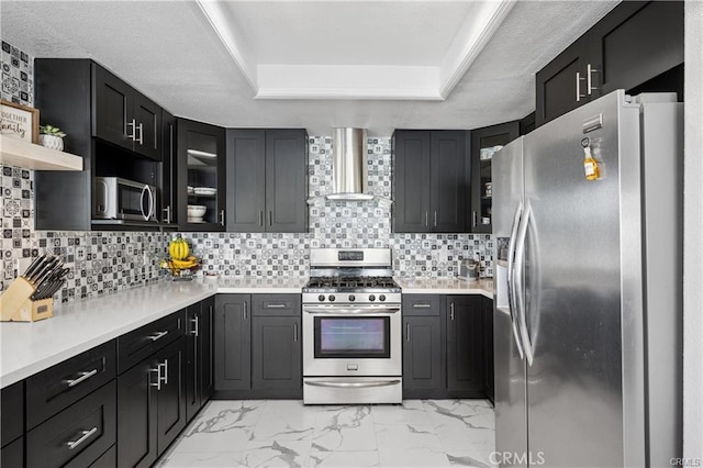 kitchen with glass insert cabinets, stainless steel appliances, light countertops, wall chimney range hood, and open shelves