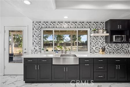 kitchen featuring marble finish floor, light countertops, stainless steel microwave, a sink, and dark cabinets