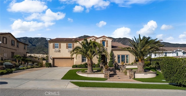 mediterranean / spanish-style home featuring a garage, concrete driveway, a tiled roof, a mountain view, and stucco siding