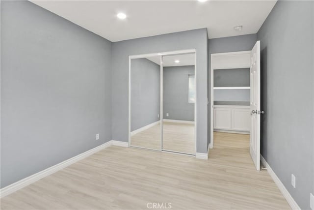 unfurnished bedroom featuring baseboards, a closet, recessed lighting, and light wood-style floors