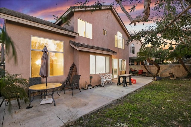 back of house at dusk with a patio and stucco siding