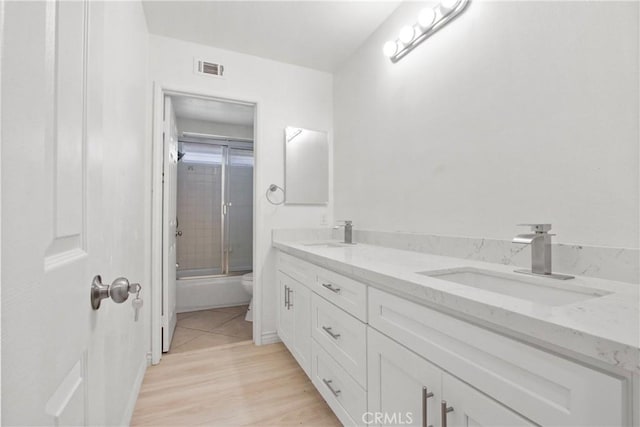 full bath featuring combined bath / shower with glass door, a sink, visible vents, and double vanity