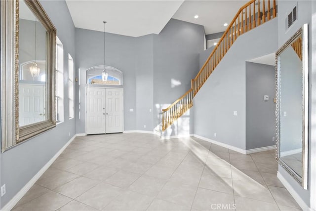 foyer entrance featuring stairs, a high ceiling, light tile patterned floors, and baseboards