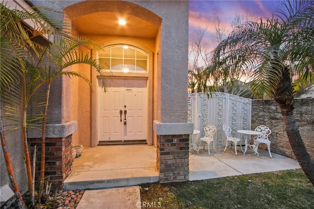 entrance to property with a patio, a gate, and stucco siding