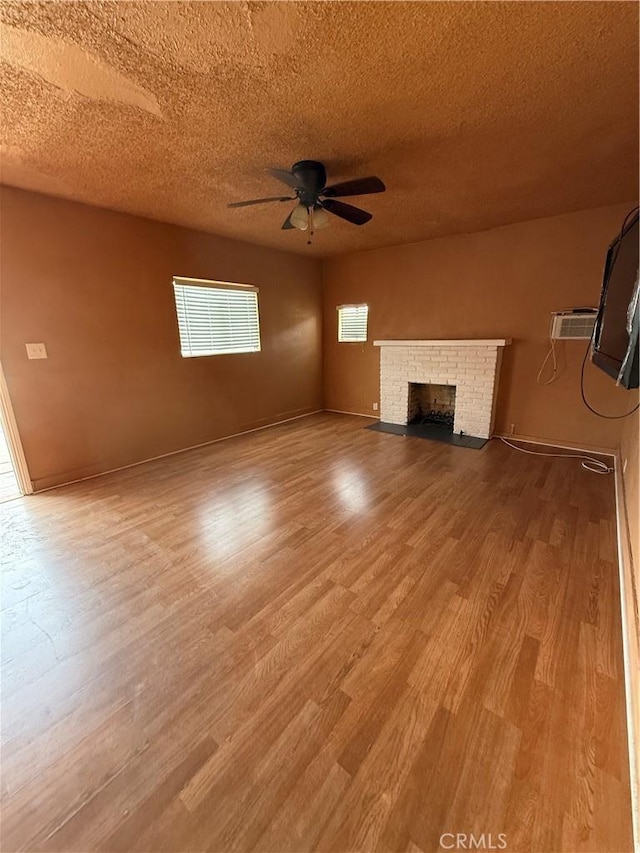 unfurnished living room with a textured ceiling, light wood-style flooring, a fireplace, a ceiling fan, and baseboards