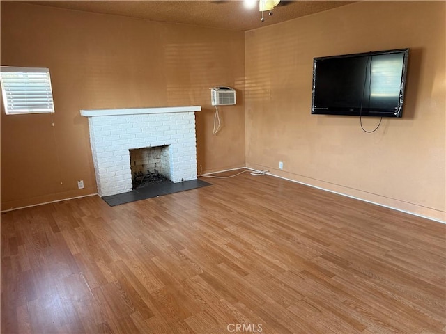 unfurnished living room featuring ceiling fan, a fireplace, wood finished floors, baseboards, and a wall mounted AC