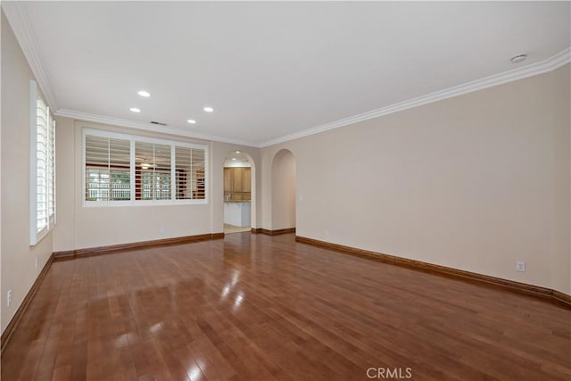 spare room featuring baseboards, arched walkways, ornamental molding, wood finished floors, and recessed lighting