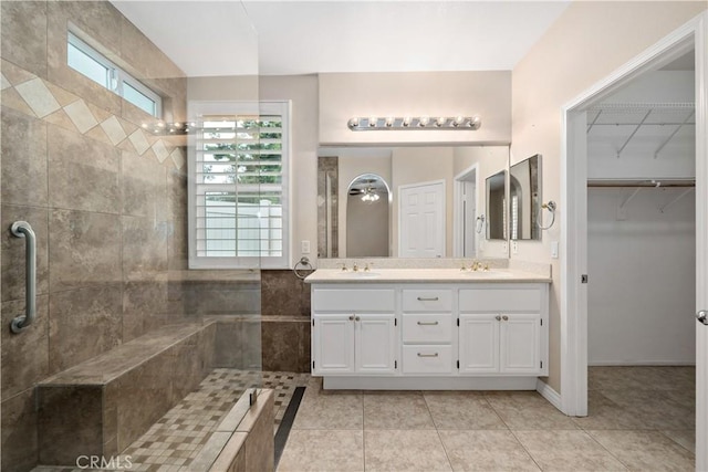 bathroom featuring tiled shower, a sink, a spacious closet, and double vanity