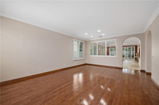 unfurnished room with arched walkways, crown molding, recessed lighting, wood finished floors, and baseboards