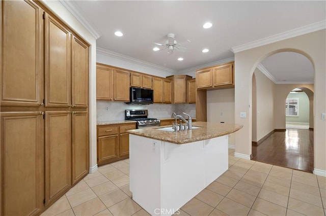 kitchen with stainless steel gas range oven, an island with sink, brown cabinets, a sink, and light tile patterned flooring