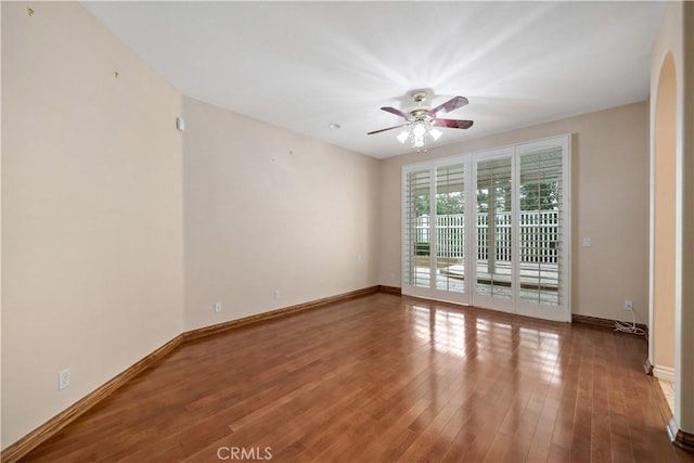 spare room with ceiling fan, arched walkways, wood finished floors, and baseboards