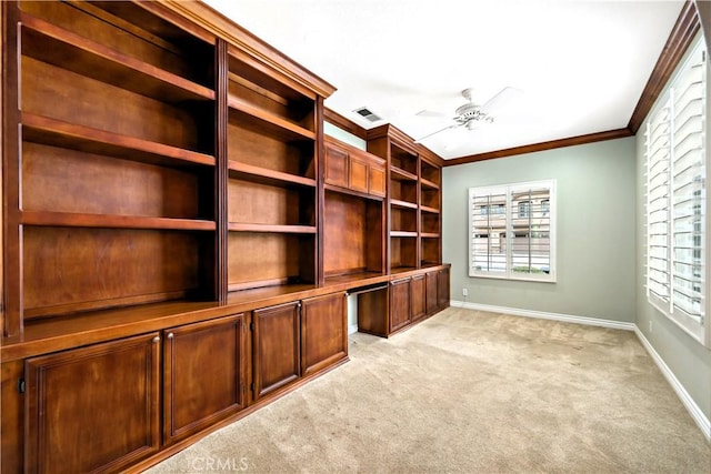 unfurnished office with crown molding, built in desk, visible vents, light carpet, and ceiling fan