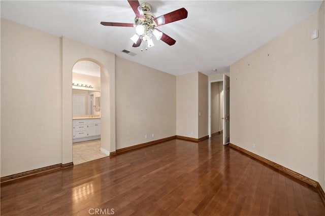 empty room featuring arched walkways, wood finished floors, visible vents, and baseboards