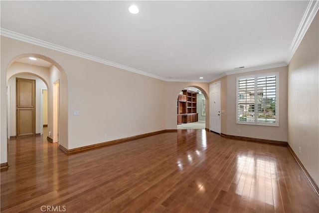 empty room featuring arched walkways, baseboards, wood finished floors, and crown molding