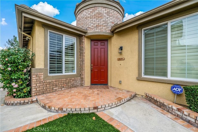 doorway to property featuring a patio area, brick siding, and stucco siding