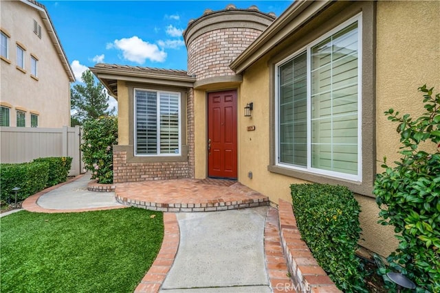 entrance to property with brick siding, a patio, stucco siding, a lawn, and fence