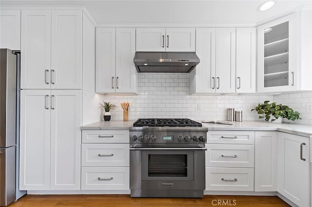 kitchen featuring light stone counters, appliances with stainless steel finishes, glass insert cabinets, white cabinetry, and under cabinet range hood