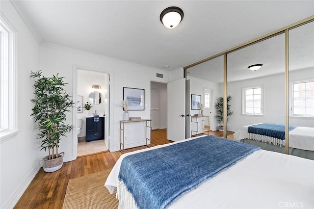 bedroom featuring a closet, visible vents, ornamental molding, wood finished floors, and baseboards