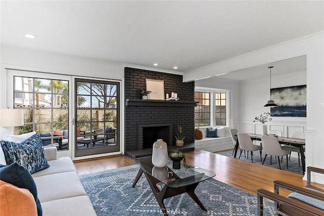 living room featuring recessed lighting, wood finished floors, wainscoting, a brick fireplace, and crown molding