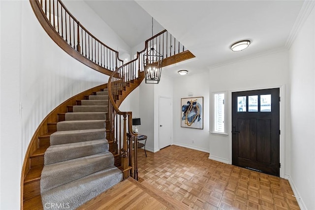 foyer entrance with ornamental molding, a towering ceiling, stairway, and baseboards